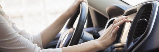 Woman in white shirt touches GPS screen on dashboard inside gray car. 